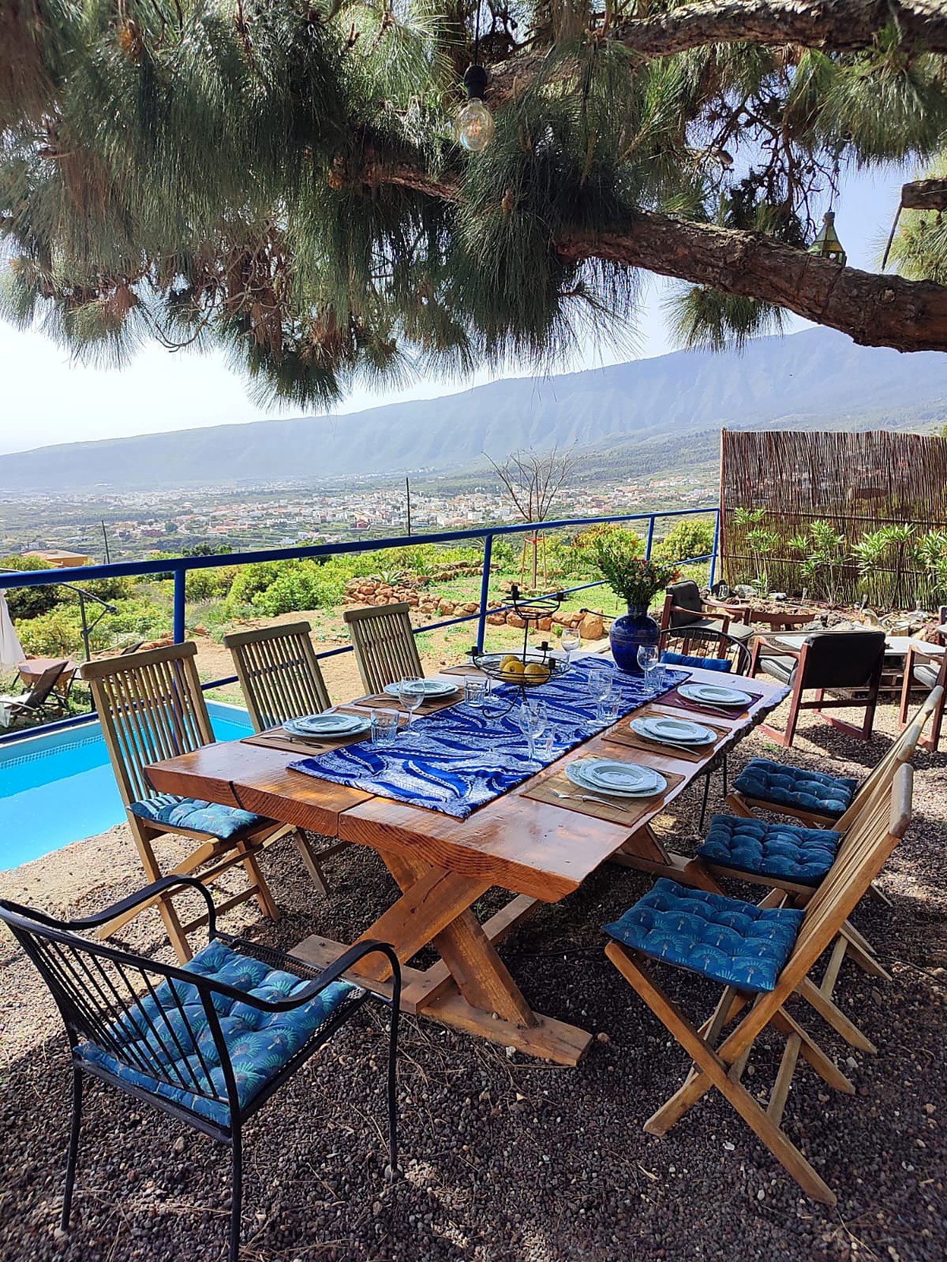 Grande table dressée sous un pin, au bord de la piscine, avec vue sur la vallée et la montagne