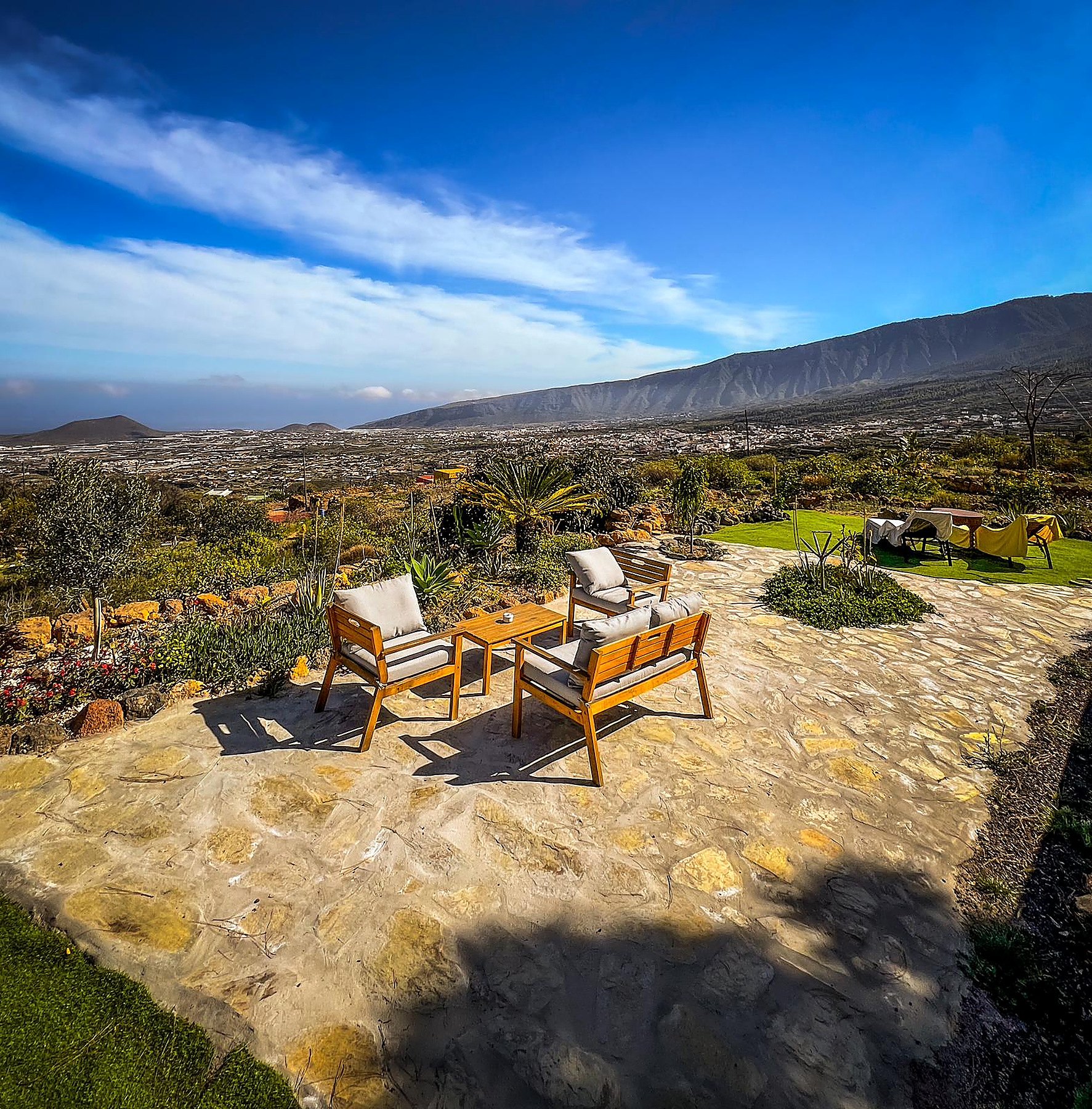 Salon extérieur en bois sur une terrasse en pierre, jardin de cactus et vue sur la vallée et la montagne