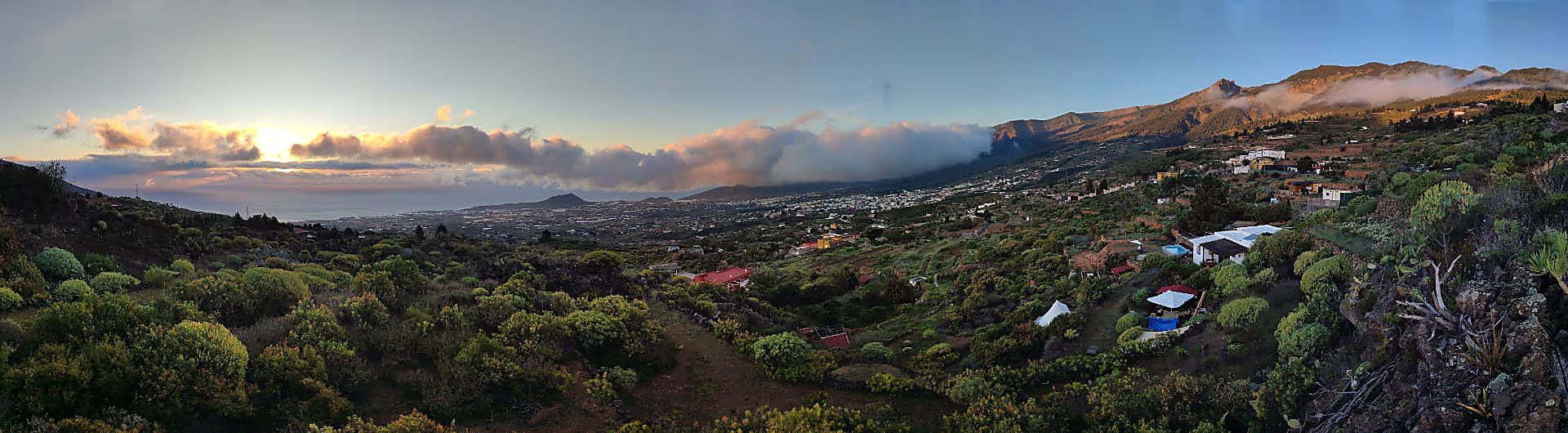Vue panoramique sur la vallée verdoyante et l'océan baignés par la lumière dorée du coucher du soleil