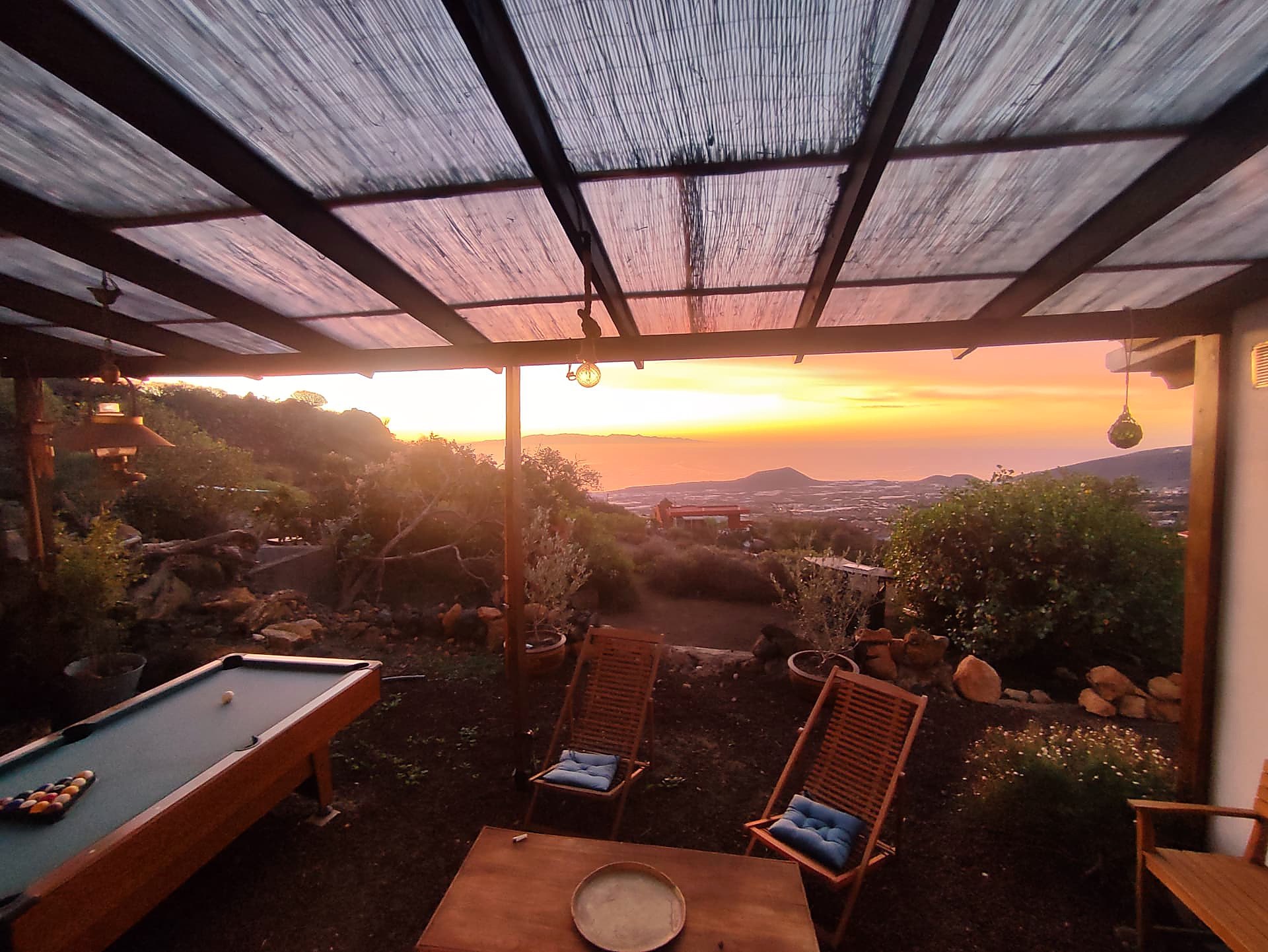Terrasse ombragée avec billard et chaises longues, face au coucher de soleil sur la vallée et l'océan