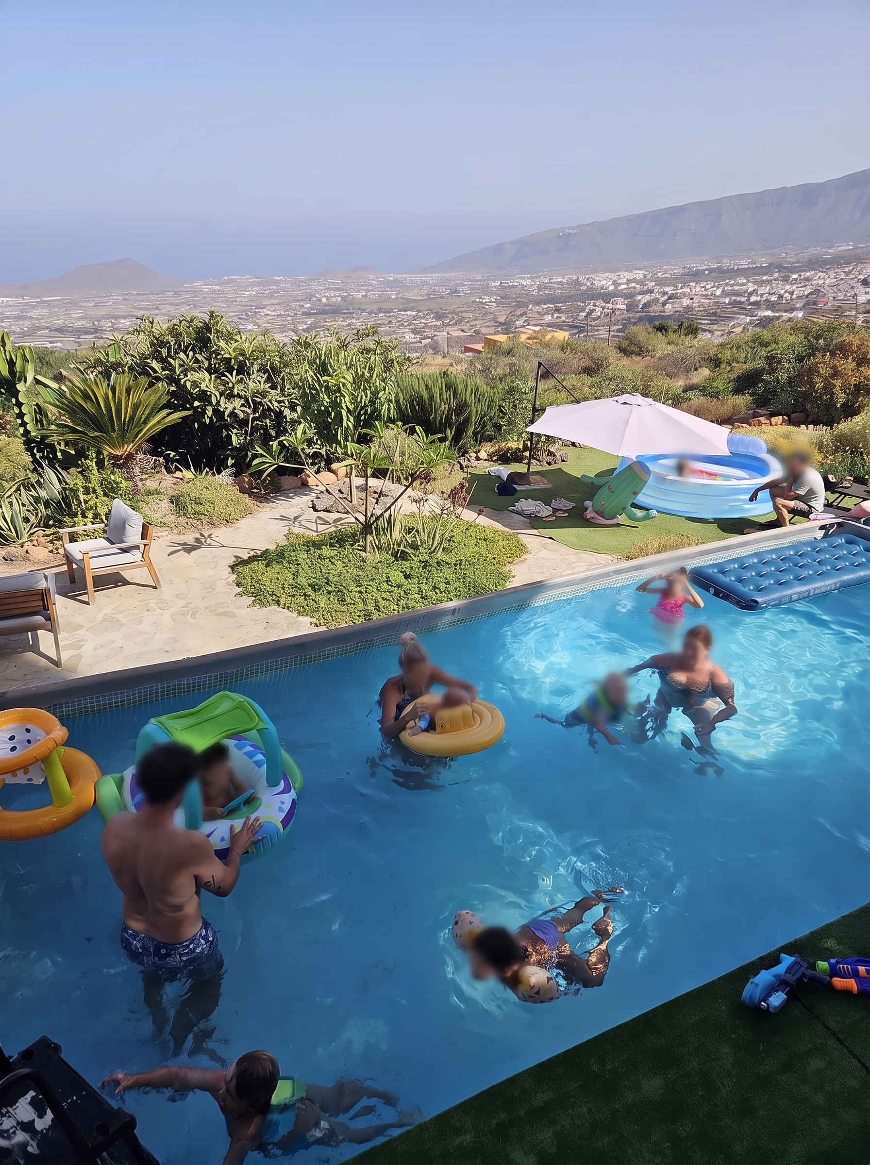 Familles et enfants qui se baignent dans la piscine, avec le jardin et la vallée jusqu'à l'océan en arrière-plan