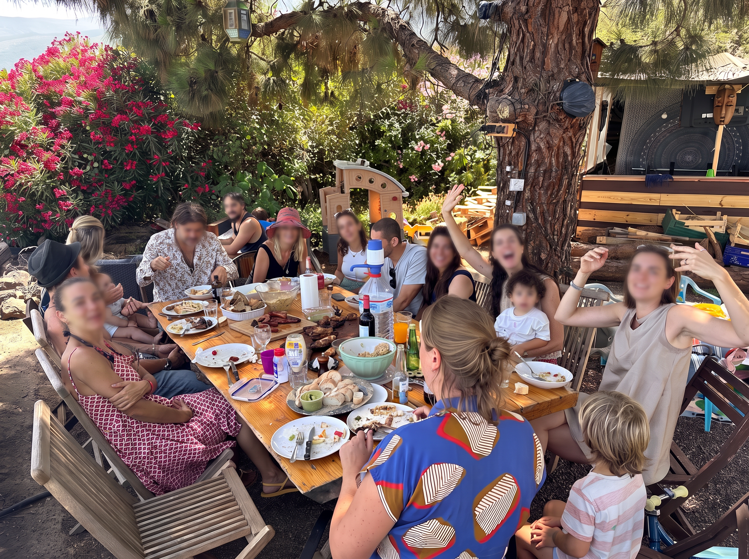 Grand repas partagé sous un pin : une longue table dressée avec une vingtaine d'assiettes, une salade et une femme riant le bras levé